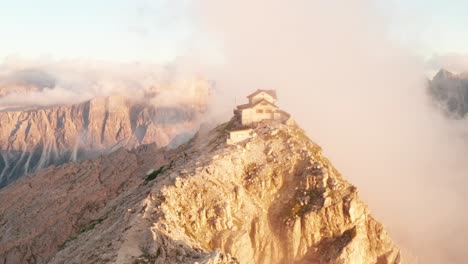 Rifugio-Nuvolau-atop-mountain-peak-lit-up-by-last-rays-of-sunset,-panoramic-Italian-Dolomites-view-from-this-mountain-lodge,-epic-aerial-view