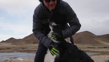 man pet happy border collie dog in icelandic rugged terrain on windy day