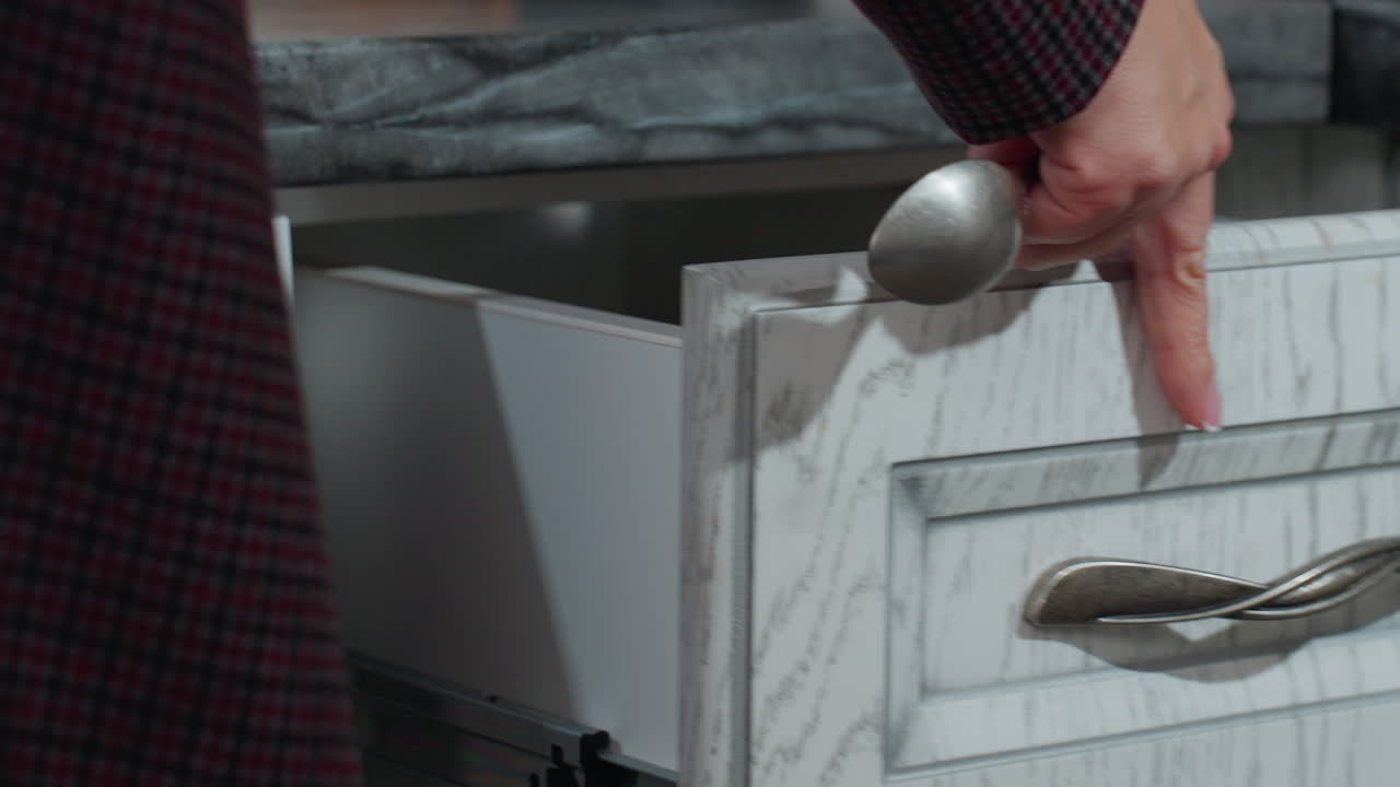 Close-up of hand in plaid clothing opening kitchen drawer, retrieving spoon, and closing it back, modern kitchen with sleek cabinetry, dishwasher, and dark countertop, efficient home organization