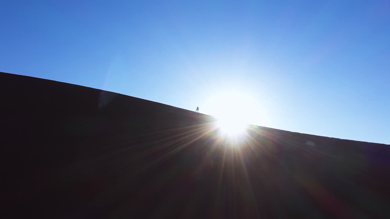 Silhouette person on top of a sand dune with a sunburst in Namibia - Aerial view