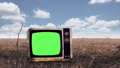 old retro television set with green screen at a rural field.