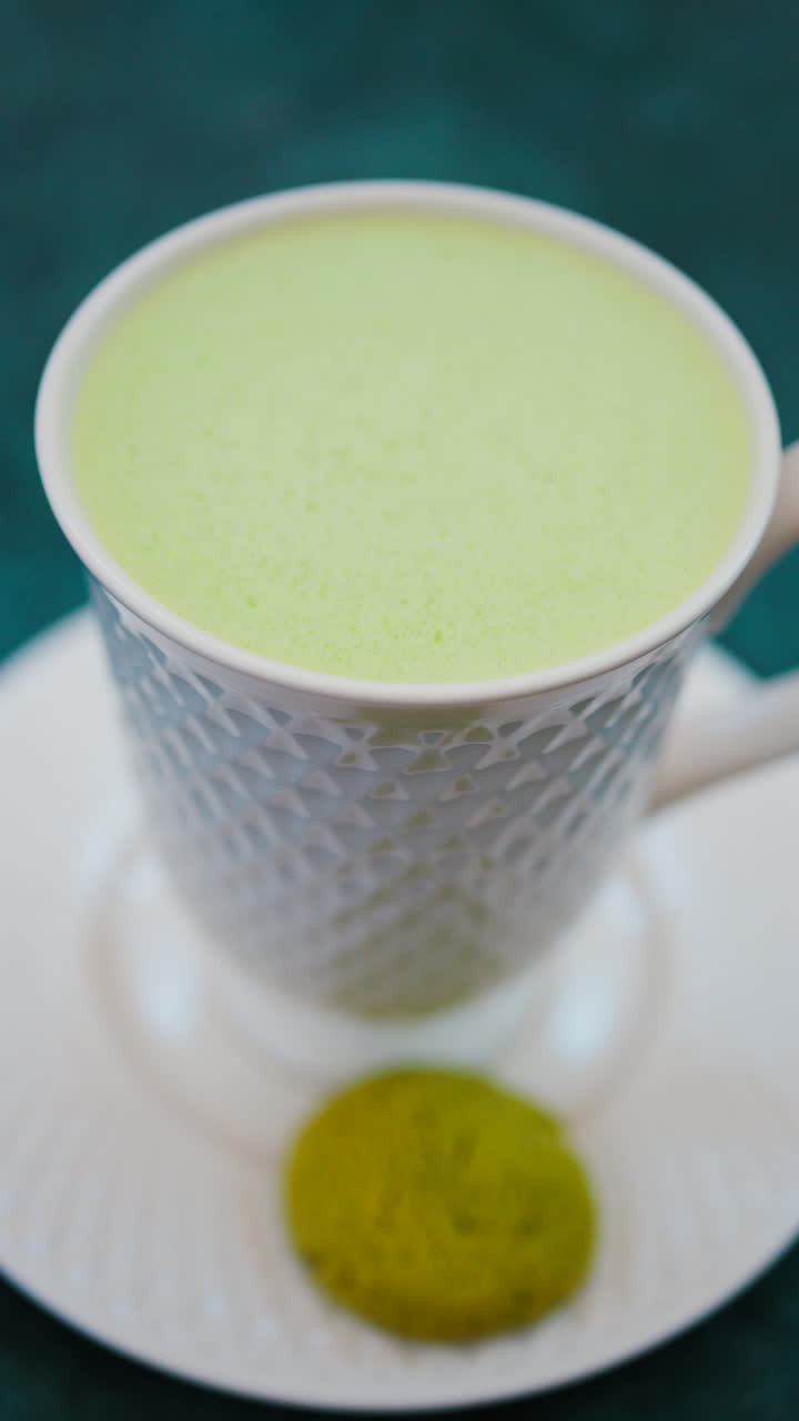Close up of a smooth matcha latte with vibrant green foam in a white cup. Vertical