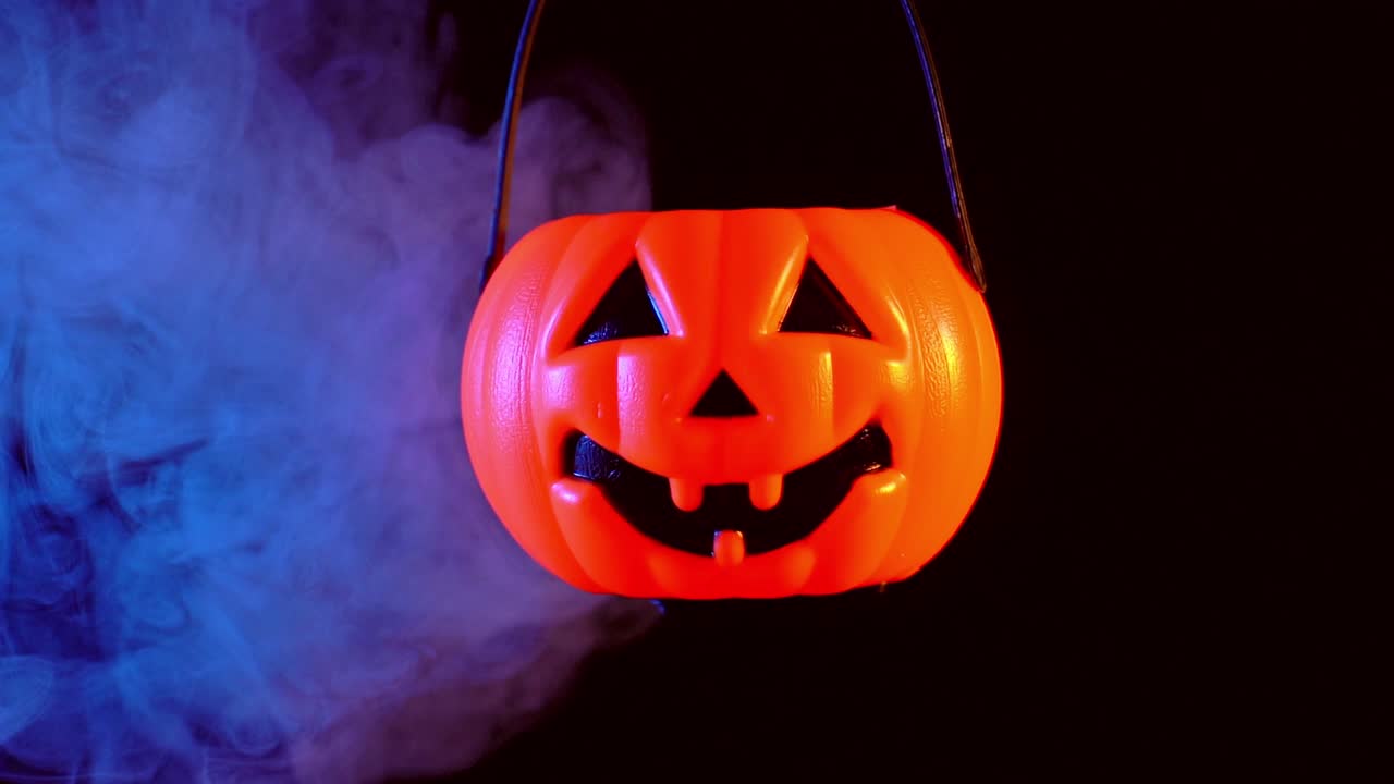 concepto de halloween - moviendo linterna de calabaza de plástico con humo azul-naranja alrededor aislado en fondo negro oscuro, aterrador y estado de ánimo de horror.