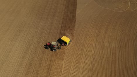 Seguimiento-De-La-Vista-Aérea-De-Un-Tractor-Rojo-De-Dos-Ruedas-Sembrando-Semillas-En-Un-Campo-Agrícola-Con-Una-Sembradora-Amarilla-Durante-La-Primavera