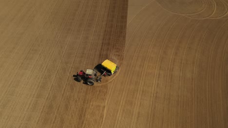seguimiento de la vista aérea de un tractor rojo de dos ruedas sembrando semillas en un campo agrícola con una sembradora amarilla durante la primavera