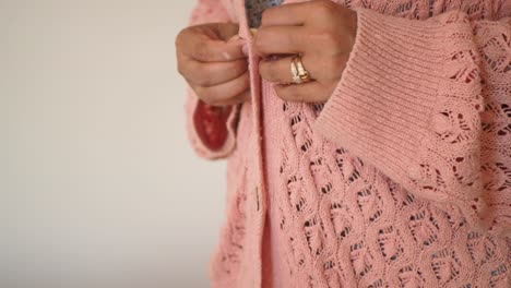 woman buttoning a pink knit cardigan
