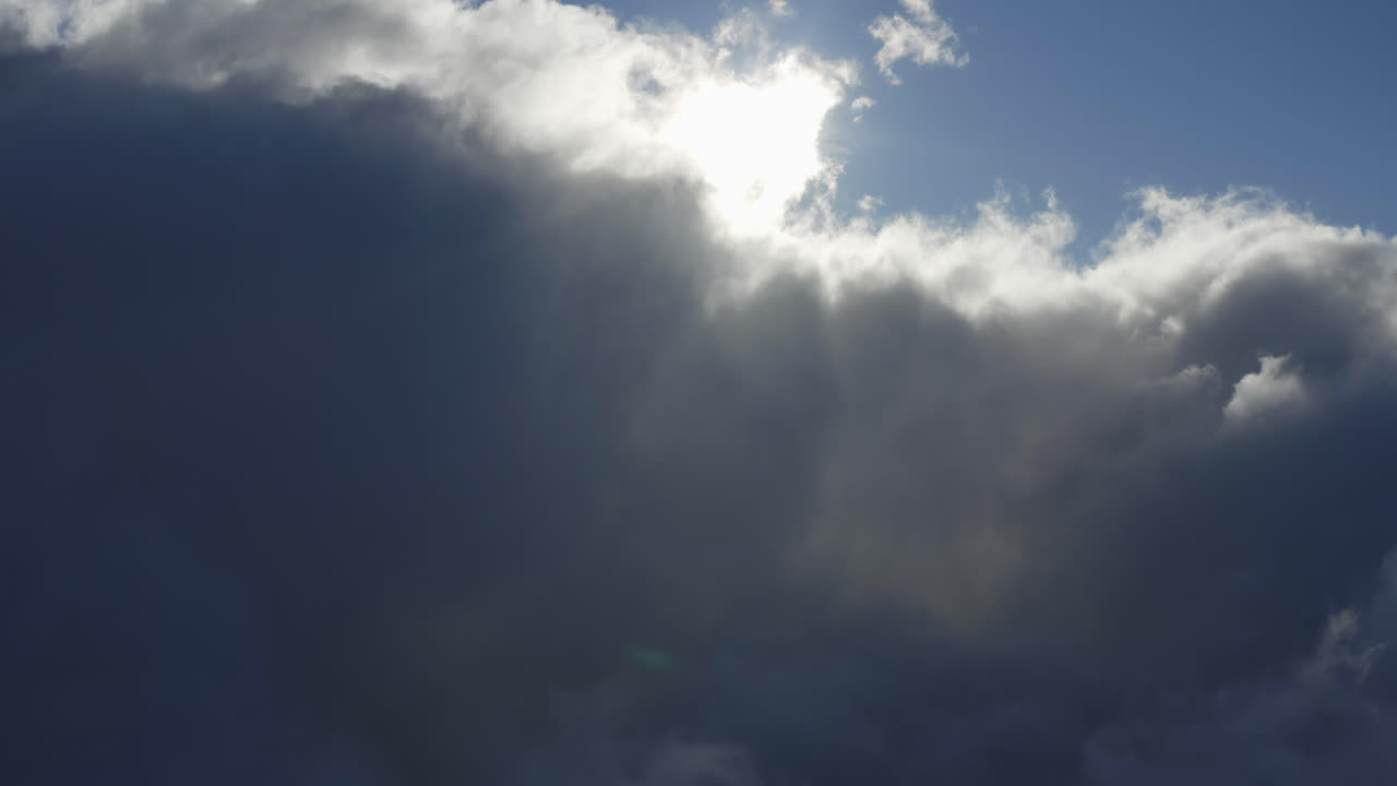 Thick cloud front rolls slowly across sky as sun rays pierce in pleasant flare