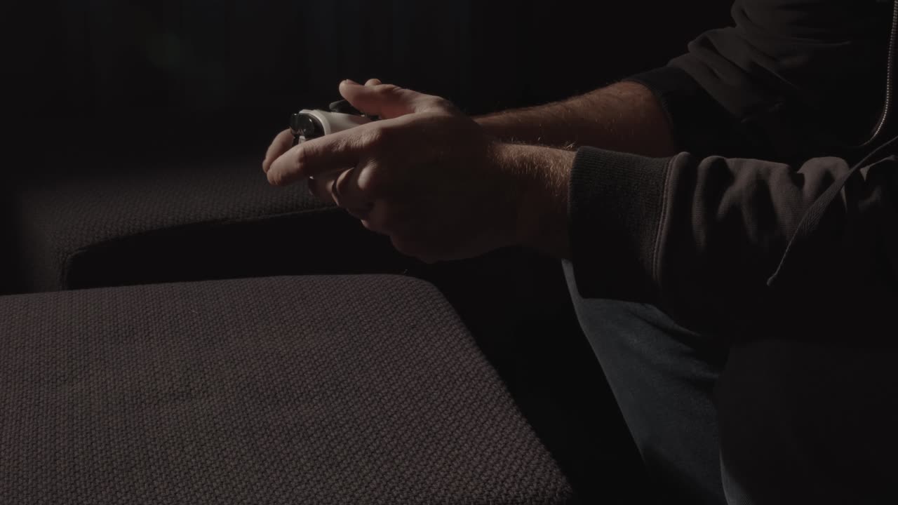 Mani maschili che giocano con un controller per videogiochi mentre la luce emessa dalla televisione lampeggia.