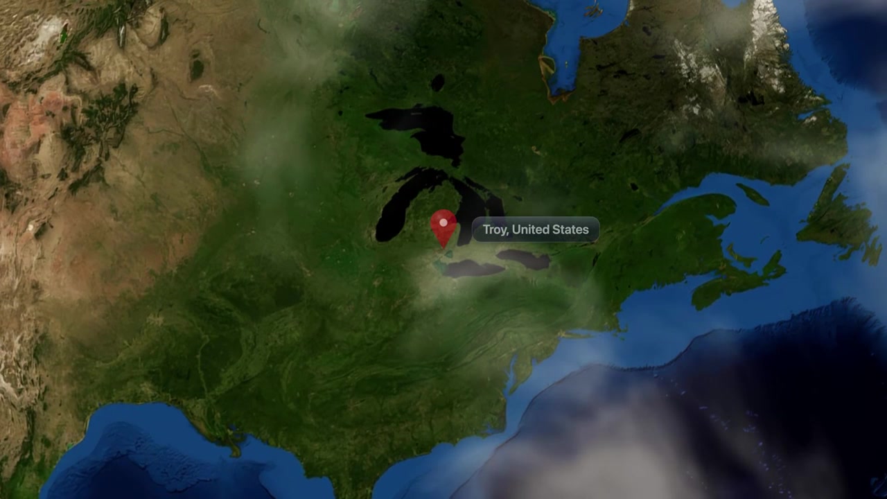Satellite view camera zooms from space into Troy, Michigan, marked by a location pin. Includes NASA public domain imagery.