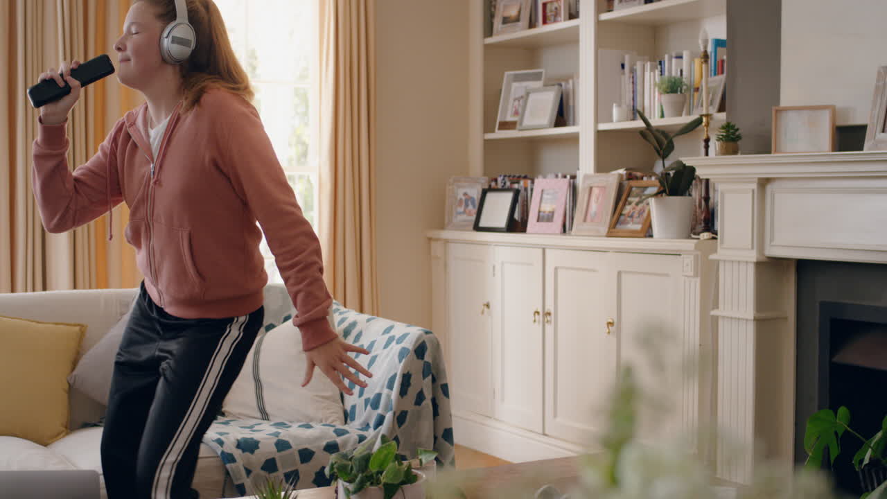 멋진 십대 소녀가 헤드폰을 착용하여 춤을 추고 음악을 듣고 재미있는 십대 소녀가 집에서 미친 춤 움직임으로 축하하고 주말에 자유를 즐기고 4k