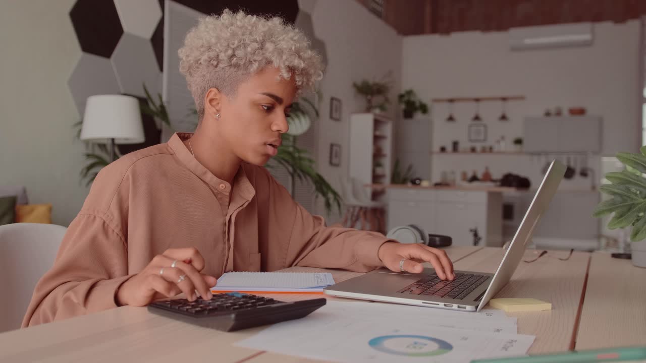 African woman calculates costs using calculator and laptop sit at home desk