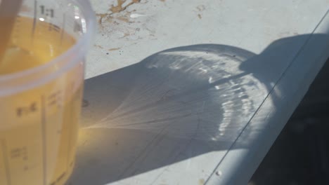 close-up of a measuring cup with yellow liquid and its shadow in sunlight