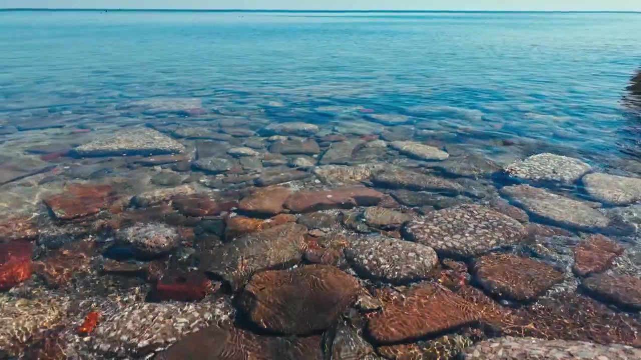 Acqua bassa che lambisce e increspa su ampie pietre piatte e rotonde in un lago blu.