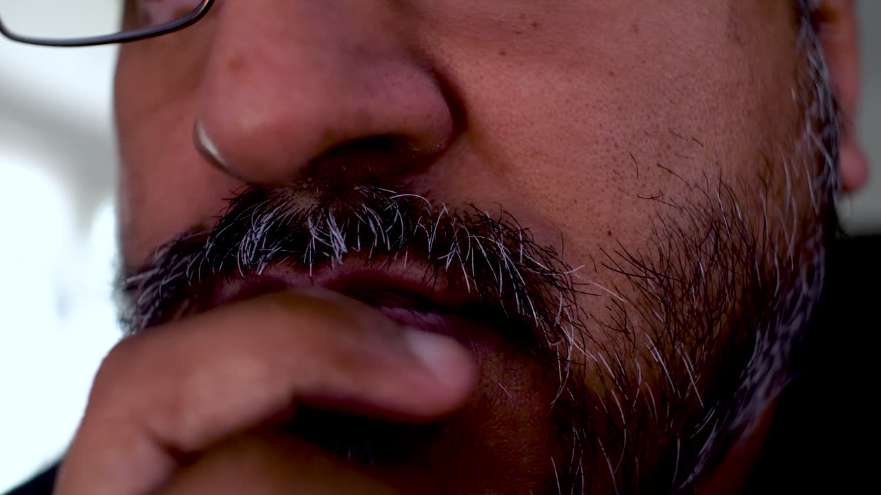Close up of a South Asian man stroking his beard deep in thought