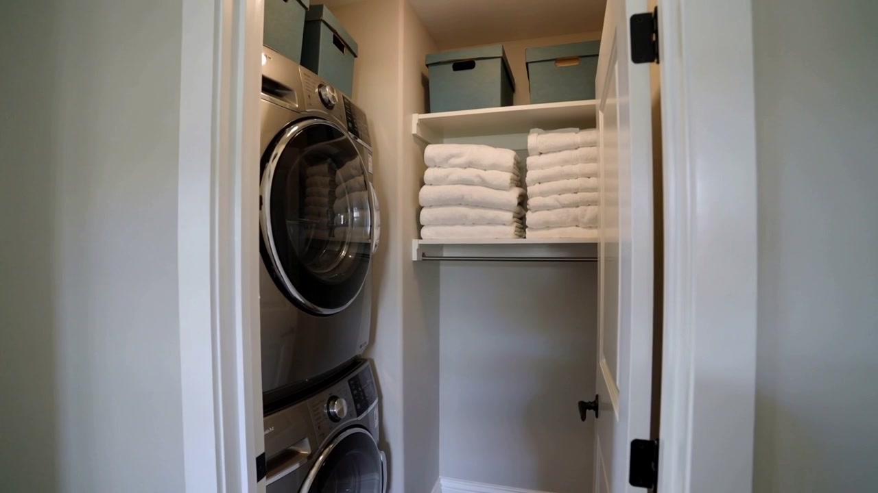 Moving camera revealing hallway closet with stacked washer dryer, light-blue bins, folded towels