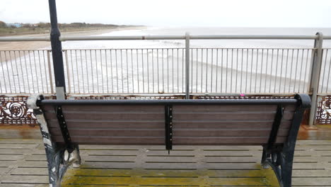 An-empty-lonely-wooden-bench-facing-the-calm-sea-on-a-pier,-with-waves-gently-lapping-the-shore