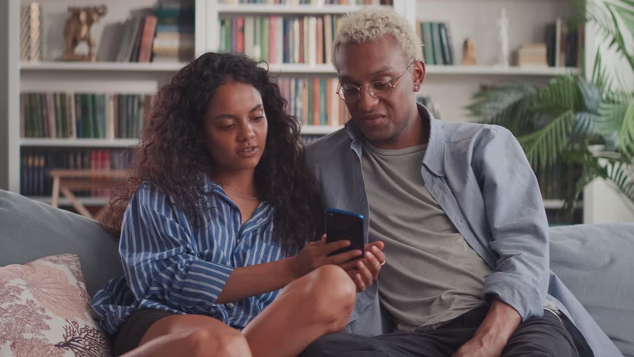 Happy young indian woman and african man hugging using smartphone together