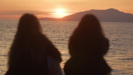two women silhouetted against a stunning sunset over the ocean