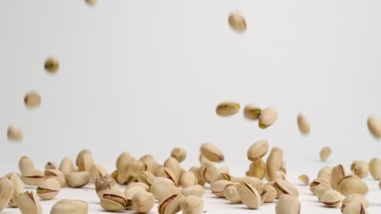 nueces de pistacho enteras con cáscara cayendo sobre la mesa blanca y rebotando a cámara lenta