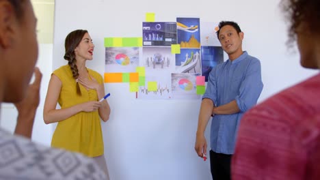 Front-view-of-Asian-male-and-Caucasian-female-executive-explaining-about-graphs-and-sticky-notes-in-