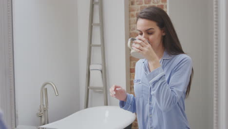woman wearing pyjamas stretches in front of bathroom mirror before running bath