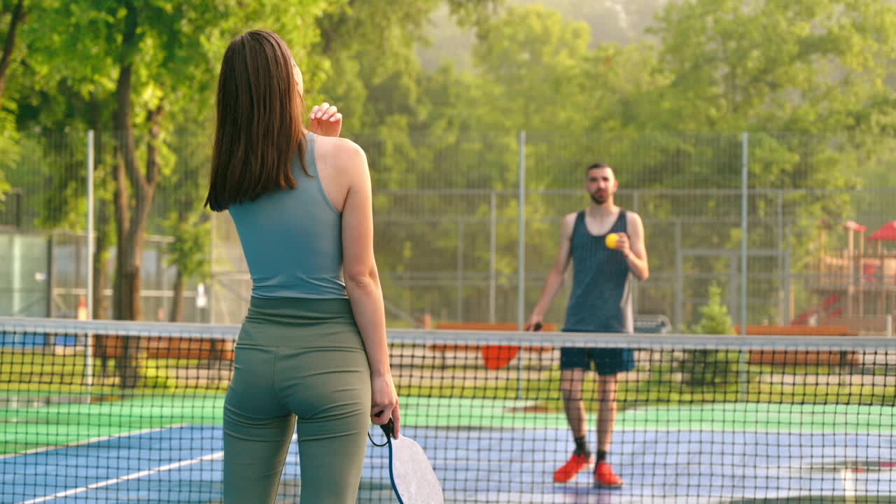 A man and a woman playing pickleball at sunrise, after rain