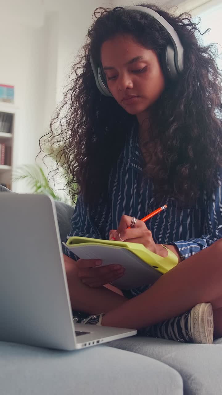 Young indian woman watching lecture on laptop and making notes in workbook