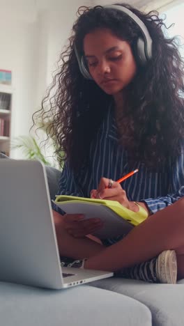 young indian woman watching lecture on laptop and making notes in workbook