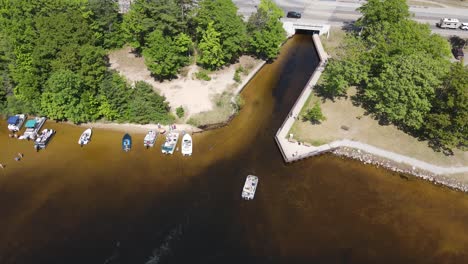 Boat-leaving-small-canal-under-highway-in-Michigan,-aerial-drone-view