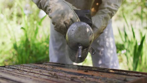 Kaukasischer-Männlicher-Imker-In-Schutzkleidung,-Der-Einen-Raucher-Verwendet,-Um-Bienen-In-Einem-Bienenstock-Zu-Beruhigen