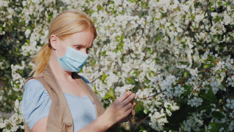 una mujer con una venda de gasa examina una flor contra un árbol floreciente problemas de enfermedades alérgicas