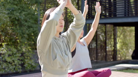 Focused-asian-female-friends-practicing-yoga-meditation-on-sunny-terrace,-slow-motion