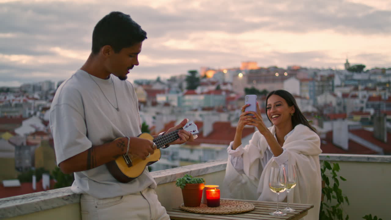 Amanti rilassati suonano la chitarra su una terrazza al tramonto. Coppia romantica che si riposa insieme.
