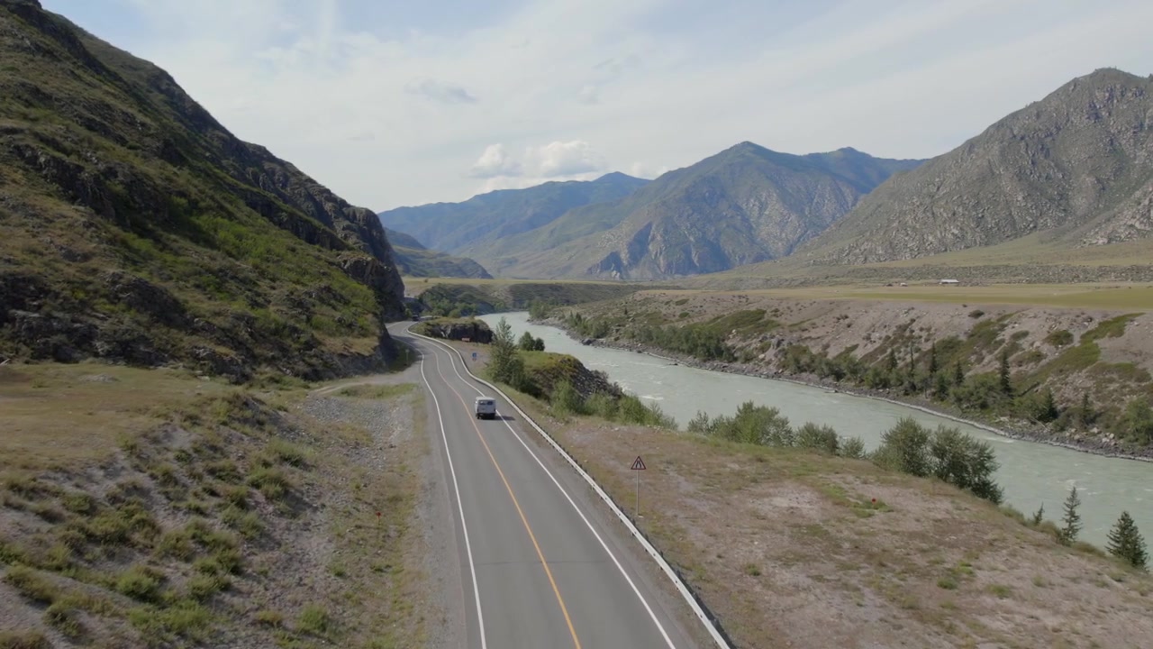 Imágenes de dron de un vehículo circulando por el Trakt Chuya junto al río Katún turquesa, rodeado de montañas escarpadas y amplios paisajes de valle en Altái, Rusia