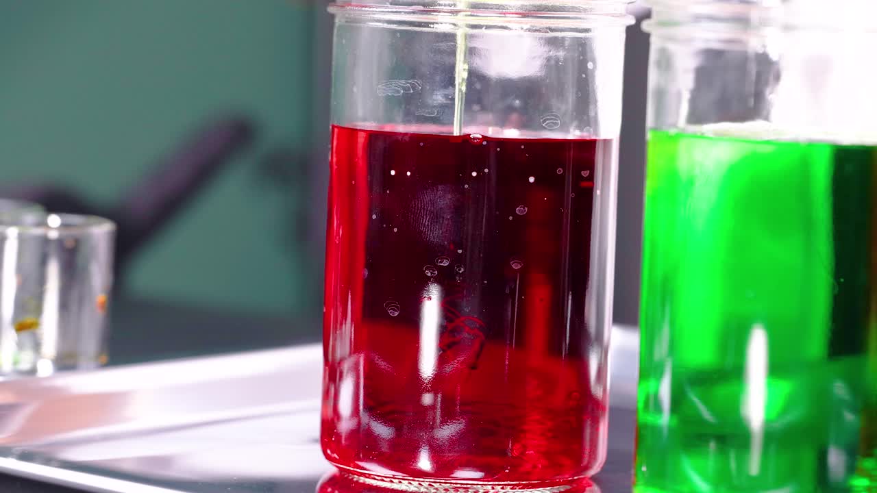 활기찬 빨간색과 초록색 액체가 유리 항아리에서 상호 작용하여 통제된 환경에서 역동적인 움직임과 색조 대조를 보여줍니다.