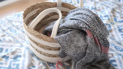 stylish straw basket with scarf on a bed