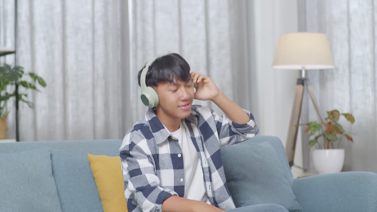 집 의 거실 의 소파 에 앉아 음악 을 듣고 춤 을 추는 헤드폰 을 착용 한 아시아 청소년 소년
