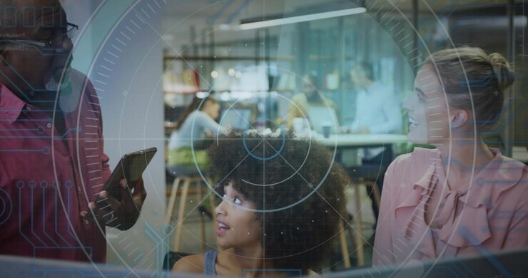 Two women working at office monitor, man approaching holding tablet showing update, HUD hovering