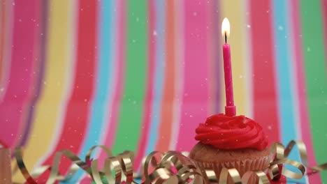 Animation-Von-Schneeflocken,-Die-über-Eine-Brennende-Kerze-Auf-Einem-Geburtstags-Cupcake-Fallen