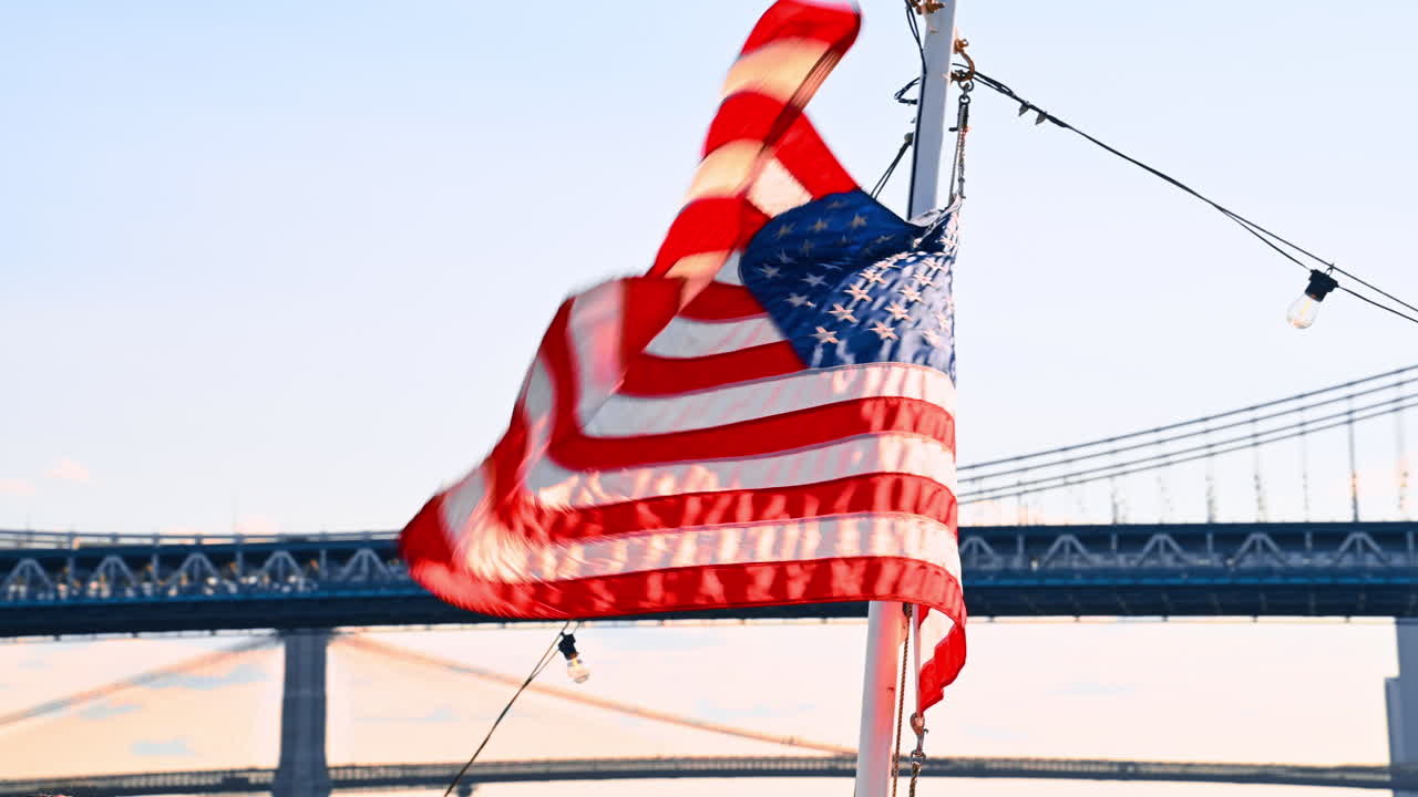 Bandiera americana al vento appesa all'albero della barca. Vista dal basso verso l'alto sul Manhattan Bridge sullo sfondo