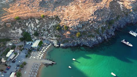 Playa-De-Agios-Pavlos-En-Rodas,-Grecia-Con-La-Acrópolis-De-Lindos,-Casas-Y-El-Mar-Mediterráneo-Durante-El-Día-Filmado-Con-El-Drone