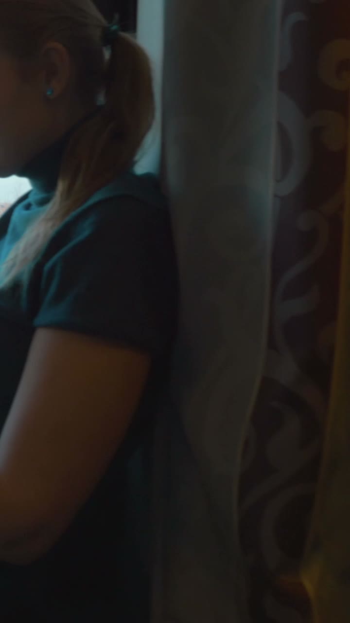 Woman looking out train window at buildings and birch trees