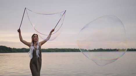 a young girl artist shows magic tricks using huge soap bubbles. create soap bubbles using sticks and rope at sunset to show a theatrical circus show