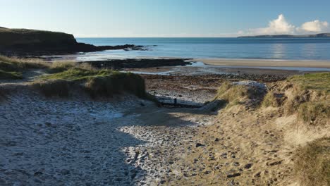 Low-flying-drone-over-frozen-sand-on-dunes-and-seaweed-covered-beach-on-a-calm-morning-with-blue-waters-of-the-ocean