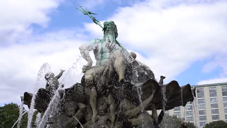 frontal shot of neptun fountain in berlin with bubbling water and blue sky with clouds in background