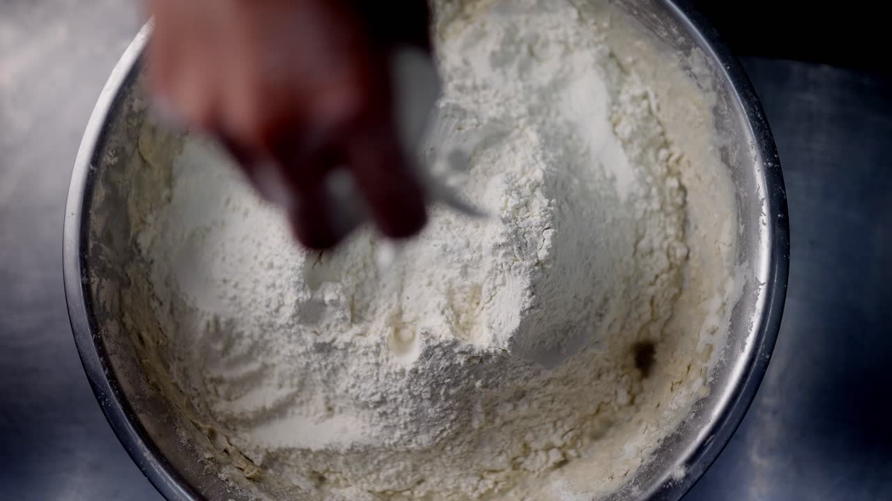 Slow motion view of a hand grabbing releasing and mixing flour in a metal bowl under cinematic and beautiful atmosphere.