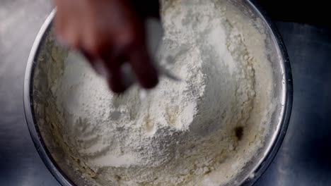 slow motion view of a hand grabbing releasing and mixing flour in a metal bowl under cinematic and beautiful atmosphere.