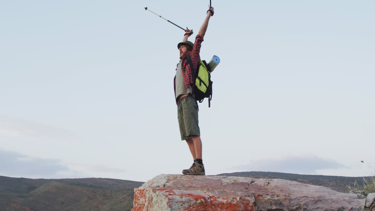 feliz sobreviviente caucásico masculino celebrando con los brazos en el aire en el pico de la montaña en el desierto