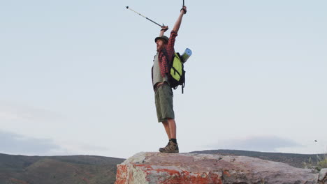 happy caucasian male survivalist celebrating with arms in the air on mountain peak in wilderness