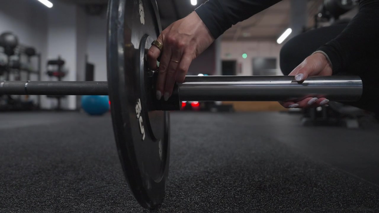 Close-up of a woman's hands sliding and securing a weight plate onto a barbell before a strength workout.